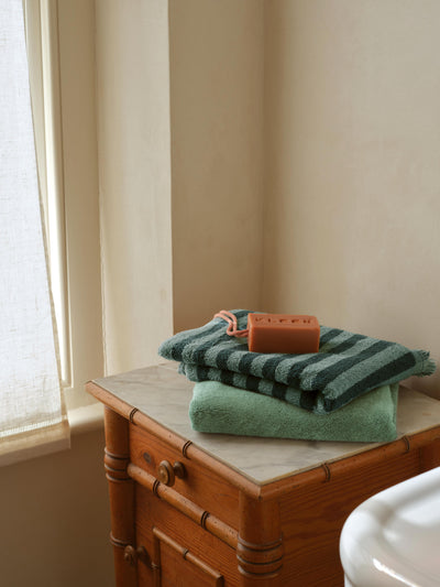 Green and striped towels on a wooden dresser with a bar of soap.