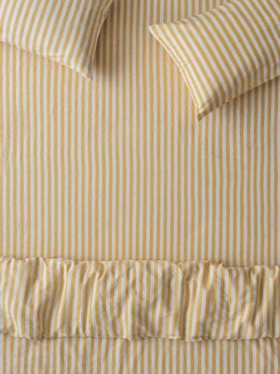 Yellow and white striped bedding set featuring a duvet cover with a ruffled hem and two matching pillowcases, shown in a flat-lay arrangement.