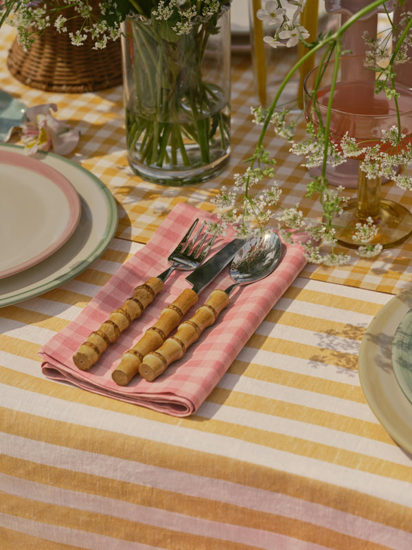 Table setting with striped tablecloth, pink checkered napkin, and floral decorations.