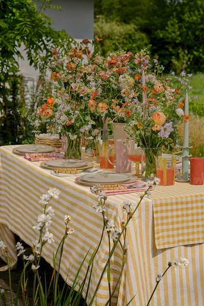 Outdoor table setting with a yellow and white checkered tablecloth, floral arrangements, and colorful glasses.