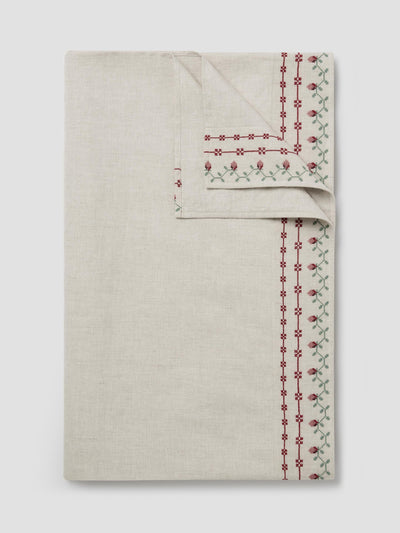 An off-white linen tablecloth with red and green embroidered borders, shown folded on a light gray background.