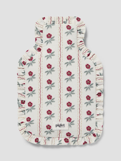 A hot water bottle cover, featuring an off-white background with vertical stripes of red flowers and green leaves, finished with a ruffled edge.