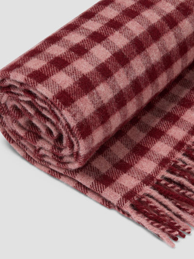 A rolled wool scarf with a classic red and pink gingham check pattern and fringed edges, shown on a neutral light gray background.