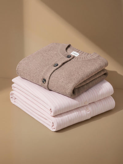 A folded knit cardigan stacked on a beige surface: a taupe cardigan on top with dark buttons, and a pale pink striped cardigan underneath.