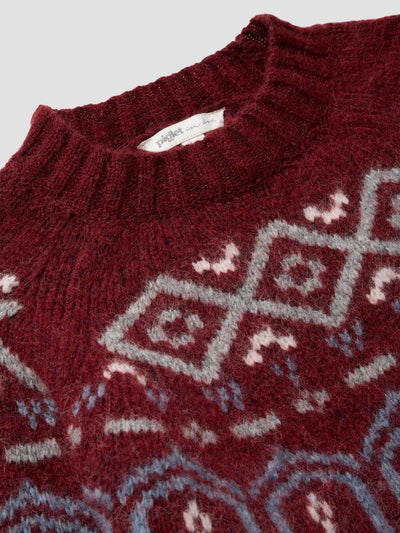 Close-up of a knit sweater in deep burgundy with a geometric diamond pattern in light gray, pale pink, and light blue. A white brand label reading 'project' is visible at the collar.